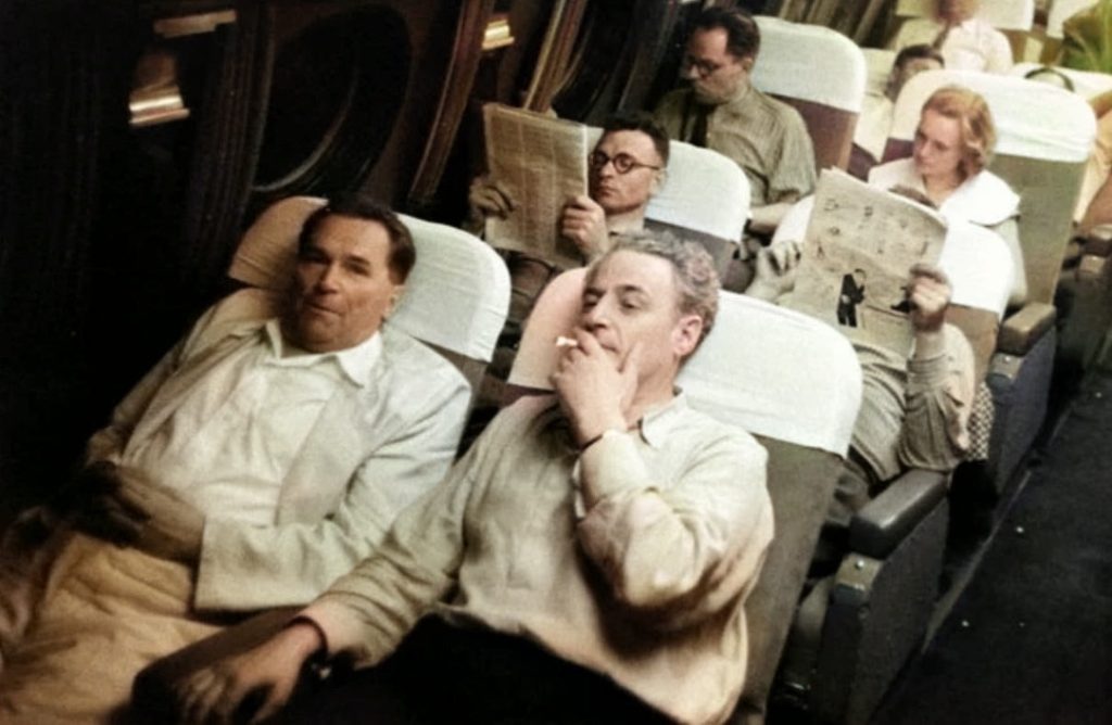Vintage airliner cabin scene with passengers and overhead lights on during cruise